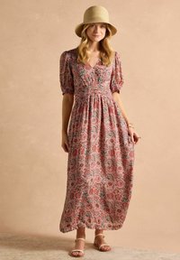 Blumiges Maxikleid in Pink mit grünen Akzenten, mit Puffärmeln, einer taillierten Taille und einem fließenden Rock. Getragen mit Sandalen und einem Strohhut.
