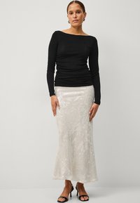 Schwarzes Langarmoberteil mit taillierter Silhouette, kombiniert mit einem silbernen, pailettenbesetzten Maxikleid mit Mermaid-Saum und strukturiertem Oberflächen.