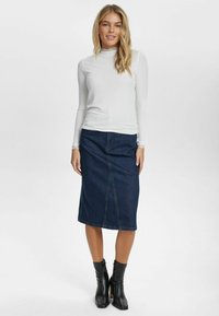 Witte blouse met lange mouwen en hoge halslijn, gecombineerd met een knielange donkere spijkerrok, zichtbare stiksels en zwarte enkellaarsjes met rits.