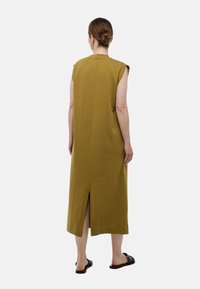 Robe maxi sans manches vert olive avec une coupe droite, dotée d'une couture au centre du dos et d'une fente à l'ourlet. Tissu texturé et léger.