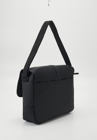 Μαύρη τσάντα ταχυδρόμου με λείο συνθετικό εξωτερικό, ρυθμιζόμενο λουράκι, φερμουάρ εμπρός τσέπης και κομψό, ορθογώνιο σχήμα.