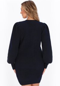 Abito in maglia blu navy con maniche lunghe a sbuffo, polsini e orlo a costine. Texture morbida, silhouette aderente e design minimalista.