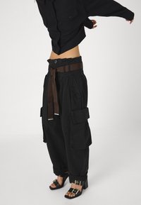 Černé cargo kalhoty s vysokým pasem, širokými nohavicemi a hnědým páskem. Mají velké postranní kapsy a texturovanou látku. Doplněny o černé sandály na podpatku.