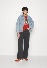 Denim jacket in light blue, red graphic tee, dark wide-leg jeans, and orange sneakers with white accents. Simple accessories.