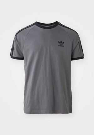 Camiseta gris de Adidas con cuello y puños de manga negros, que presenta el logotipo de Adidas en negro y tres rayas negras en cada hombro.