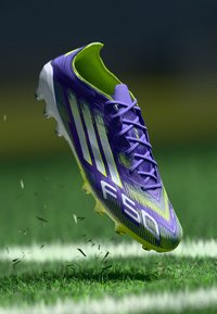 Sports cleat featuring a purple and neon green design, textured upper with diagonal stripes, and lightweight sole with visible studs.
