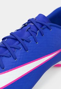 Μπλε ποδοσφαιρικό παπούτσι με υφή στην επιφάνεια, λεπτές ροζ και λευκές λεπτομέρειες, και τυπικό σύστημα κορδονιών. Ο σχεδιασμός εστιάζει στην απόδοση και την ευελιξία.