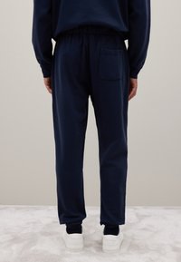 Marineblaue Sweatpants mit einem elastischen Bund, gerippten Knöcheln und einer Gesäßtasche. Hergestellt aus einem weichen Material, kombiniert mit weißen Sneakers.