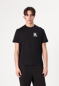 Black cotton t-shirt featuring a small white CK Calvin Klein logo on the left chest. Short sleeves and a crew neckline.