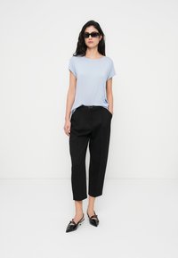 Φωτεινό γαλάζιο κοντομάνικο τοπ, μαύρο ψηλόμεσο παντελόνι κομμένο πάνω από τον αστράγαλο, και μαύρα παπούτσια με μυτερή μύτη, με στρογγυλά γυαλιά ηλίου και ίσια μαλλιά.