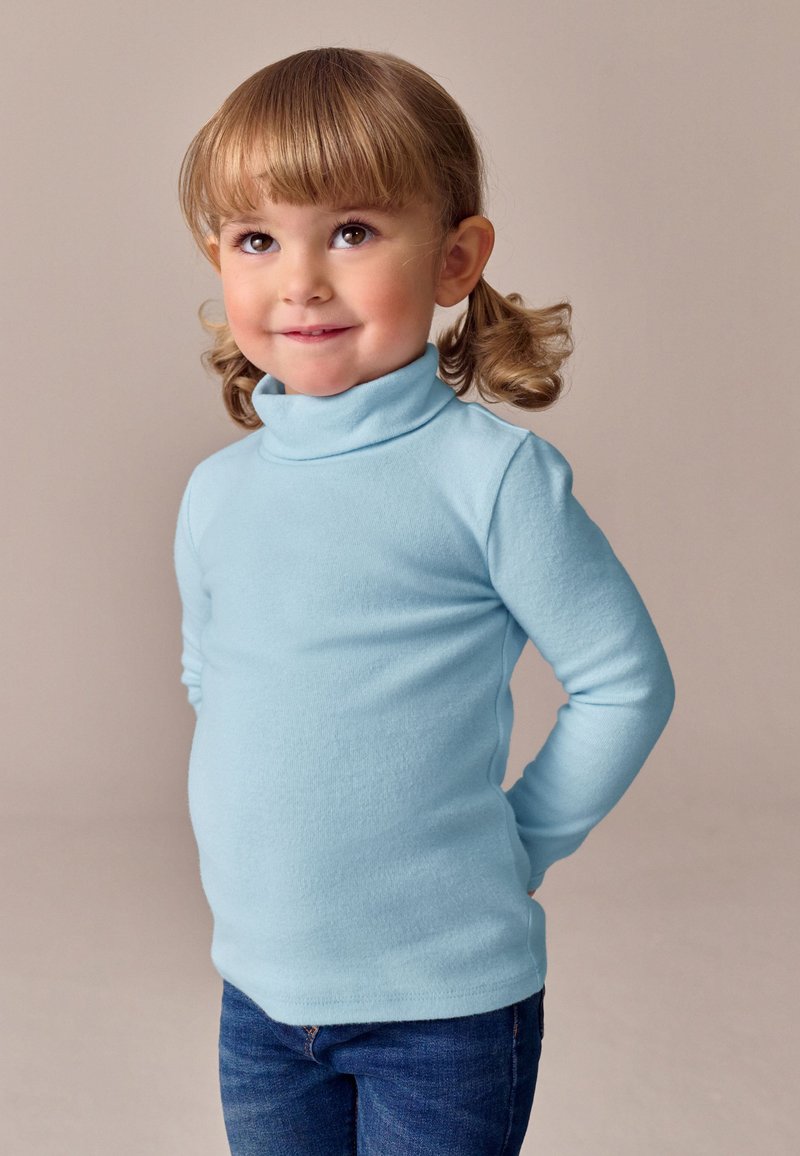 Suéter de cuello alto azul claro hecho de tela suave, mangas largas, diseño ajustado, combinado con vaqueros oscuros.