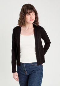 Cardigan noir en tricot côtelé avec ouverture à l'avant et manches longues, porté par-dessus un débardeur blanc. Présente une coupe ajustée et une texture douce.