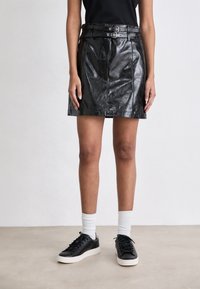 Gonna mini in pelle nera con vita con cintura, cuciture dettagliate e una texture lucida, abbinata a sneakers nere e calze bianche.