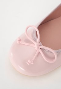 Ballerines roses avec une finition brillante, présentant un bout arrondi et un nœud noué à l'avant. Texture lisse et bord élastique.