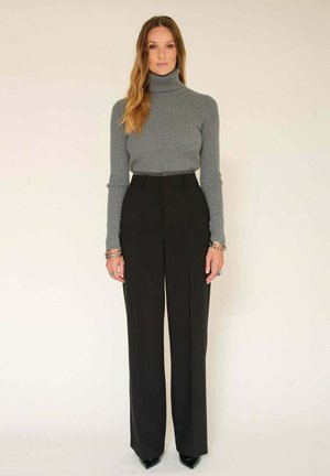 Un pull à col roulé côtelé gris associé à un pantalon noir à taille haute et à jambes larges. La tenue est complétée par des escarpins noirs à bout pointu et des accents en bijoux en argent.