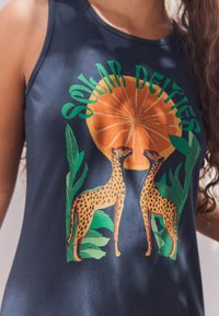 Tumesinine maika, millel on graafiline kujundus kahe gepardi ja apelsiniga, ümbritsetud rohelise lehestikuga. Pehme kangas ja mugav lõige.