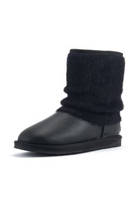 Bottine noire avec une base en cuir lisse et un tour de cheville en laine douce et duveteuse. Bout rond et semelle en caoutchouc plate avec des détails de couture minimalistes.