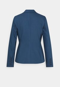 Blazer azul a medida con solapa muestrada, corte estructurado y mangas largas con cuatro botones en los puños. Textura de tela suave.