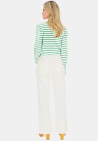 Białe spodnie z szerokimi nogawkami w połączeniu z zieloną i białą bluzką w paski z długim rękawem. Stylizacja charakteryzuje się luźnym krojem i gładką fakturą materiału.
