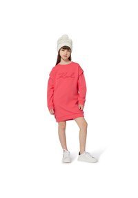 Rosa sweatshirt-kjole med oversized passform, ribbestrikkede mansjetter og kant. Har "Karl" brodert i kursiv. Hvit strikket lue og hvite joggesko.