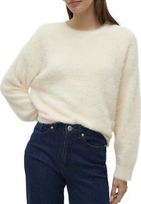 Un pull en crème duveteux avec un col rond et des manches longues, associé à un jean en denim bleu foncé, présentant un design classique à cinq poches.
