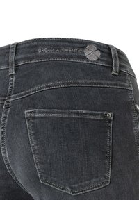 Los vaqueros de mezclilla de lavado oscuro presentan una textura suave, un desvanecimiento sutil, un diseño de cinco bolsillos y un logo bordado "DREAM AUTHENTIC" en la parte trasera.