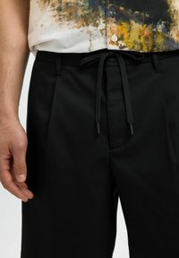 Černé kalhoty na míru s hladkým povrchem, vybavené stahovacími šňůrkami v pase. Materiál je lehký a vhodný pro volnočasové nošení.