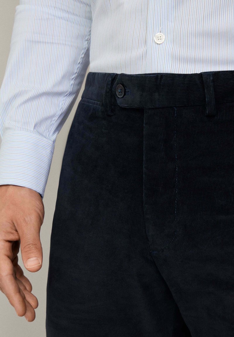 Pantalons en velours côtelé bleu marine foncé avec une finition texturée, dotés d'une fermeture à bouton, de poches latérales et d'une coupe droite.