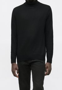Black turtleneck sweater made of a soft knit fabric, featuring a slim fit, ribbed cuffs, and hem, paired with dark jeans.
