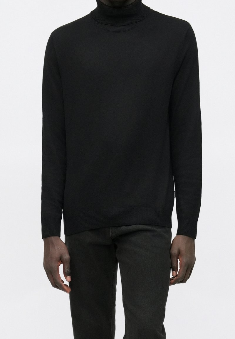 Black turtleneck sweater made of a soft knit fabric, featuring a slim fit, ribbed cuffs, and hem, paired with dark jeans.