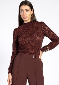 Bordeaux kanten top met een hoge hals en lange mouwen, voorzien van bloemmotieven en ruches. Gecombineerd met donkerbordeaux hoge taille broeken.