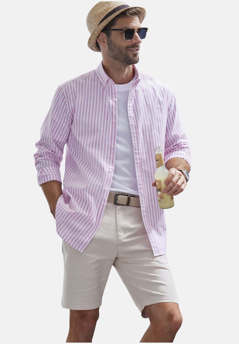 Hellbraunes und weiß gestreiftes Hemd mit Knöpfen, darunter ein weißes T-Shirt, beige Shorts, silberner Gürtel, Strohhut und Sonnenbrille. Hält ein Getränk.