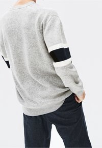 Šedý pletený svetr s kontrastními tmavě modrými a bílými pruhy na rukávech, s texturovaným povrchem a žebrovaným lemem.