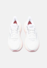 Ζευγάρι λευκά παπούτσια τρεξίματος Saucony με ροζ άκρες σόλας, πανί στο πάνω μέρος και κορδόνια, εμφανιζόμενα από πάνω σε φωτεινό φόντο.