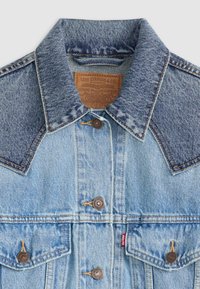 Veste en denim bleu clair avec un empiècement bleu foncé contrastant, boutons en cuivre, deux poches avant et une étiquette de marque en cuir à l'intérieur du col.