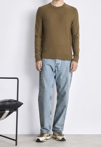Pull en tricot marron avec poignets et ourlet côtelés, associé à un jean droit bleu clair et des chaussures de sport beiges. Détails minimaux sur le pull.