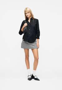 Jeune femme portant une chemise noire boutonnée, une mini-jupe à carreaux noir et blanc, des chaussettes blanches, des talons noirs et un sac à bandoulière clouté.