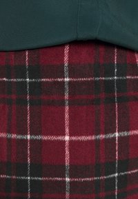 Tissu vert chevauchant un tissu en laine à carreaux rouge, noir et blanc avec un motif à damier.