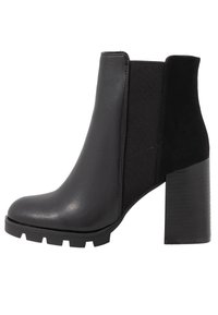 Mustat nilkkurit, jotka on valmistettu sileästä nahasta ja mokkasta. Niissä on paksu korko ja joustavat sivupaneelit, jotka helpottavat pukemista. Paksupohjaiset uritetut pohjat.