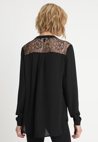 Blusa nera a maniche lunghe con pannello posteriore in pizzo floreale, tessuto satinato, colletto da camicia e polsini con bottoni, con fessure laterali all'orlo.