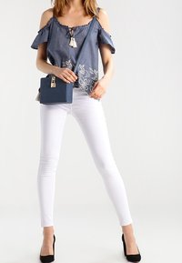 Denim off-shoulder top med blomsterbroderi; parret med tætsiddende hvide jeans og sorte højhælede sko; lille blå crossbody taske.