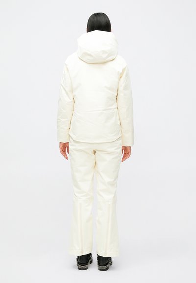 Fehér szigetelt kabát kapucnival és hozzáillő nadrággal. Az anyag sima, enyhén fényes, hideg időjárásra tervezett, a nadrág cipzárral ellátott.