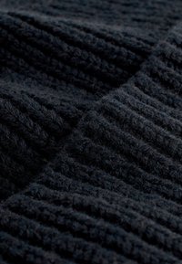 Teksturirana crna tkanina s rebrastim uzorkom, prikazujući meku, pahuljastu površinu i varijabilne debljine kroz cijeli materijal.