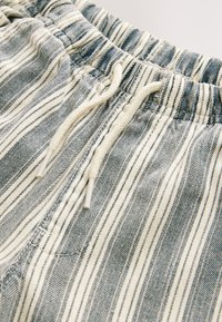 Szorty w paski w kolorze niebieskim i kremowym, z elastycznym pasem i sznurkiem oraz bocznymi kieszeniami. Tkanina ma miękką teksturę.