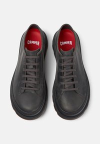 Černé ležérní tenisky se šedými tkaničkami a červenou vložkou, na které je výrazně zobrazeno jméno značky "CAMPER".