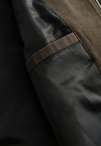 Interior de una chaqueta de ante marrón y nylon negro, que presenta una textura suave, un diseño bicolor y costuras reforzadas a lo largo de las uniones.