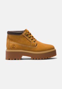 Bruine suède enkelboots met gele en rode veters, een gevoerde kraag en een dikke rubberen zool met diepe profielgroeven.