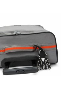 Gray travel bag with a durable exterior, orange accent strap, a retractable handle, and a distinctive black monkey-shaped tag.
