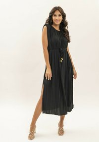 Robe midi plissée noire avec encolure ronde, taille nouée, fentes latérales et accents en perles jaunes ; texture douce et design fluide.
