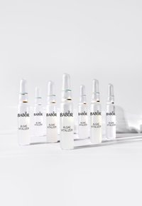 Set of eight transparent glass vials containing "Algae Vitalizer" from BABOR, featuring white liquid and silver or green accents on the caps.